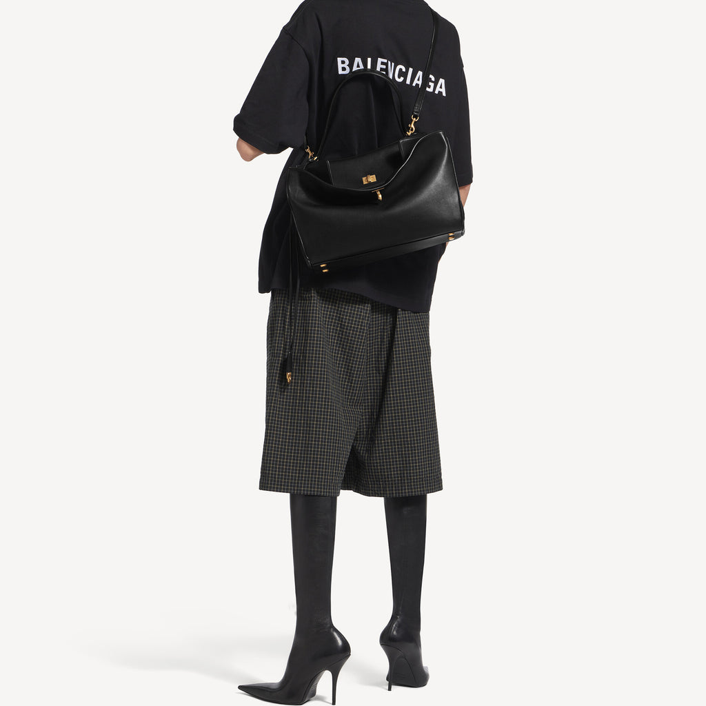 A model wearing a Rodeo style slouchy medium tote bag in black with brassy gold hardware