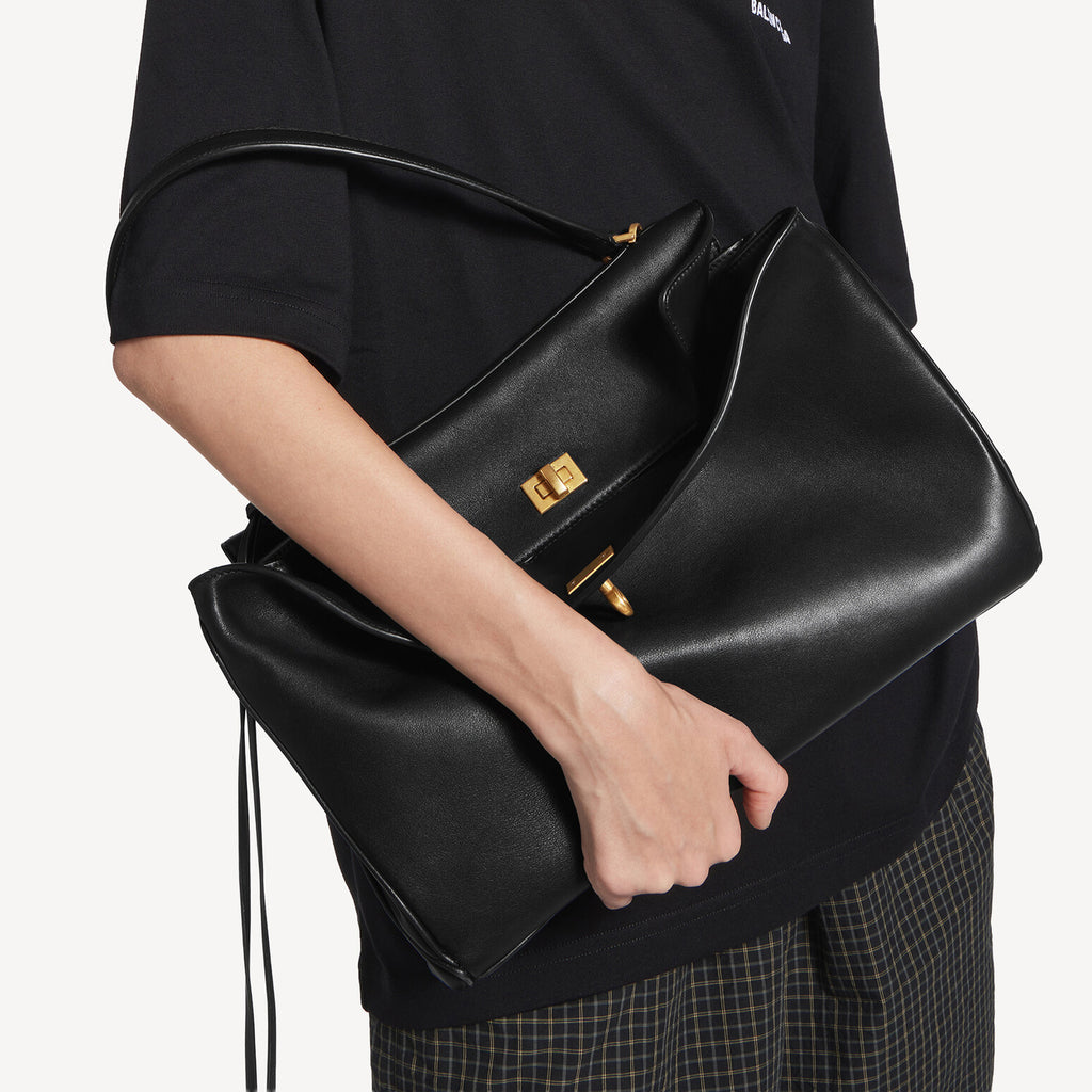 A model holding a Black Rodeo inspired leather tote with gold hardware featuring a relaxed rectangular silhouette.
