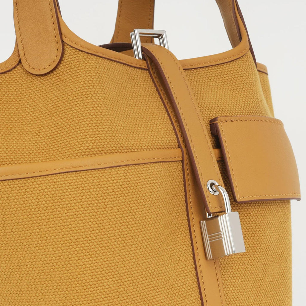 Sesame Beige bucket bag with canvas-style body, vegan leather trim, top-handle, lock strap, and utility side pockets