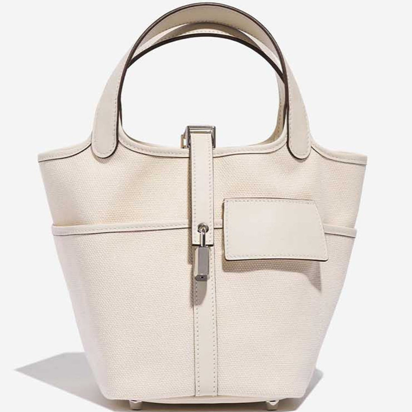 White canvas bucket bag with top handle and structured shape with silver lock
