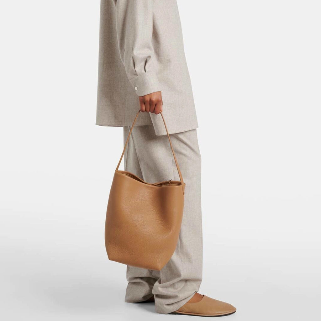 Model holding camel the N/S Park style medium vertical tote in genuine leather, showcasing its clean rectangular silhouette.