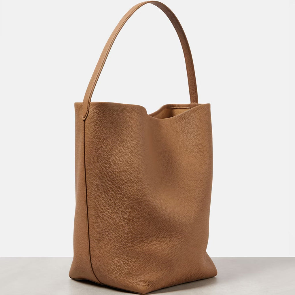 Large vertical tote bag in warm brown vegan PU leather with soft structure, minimalist design, and wide shoulder straps for everyday wear.