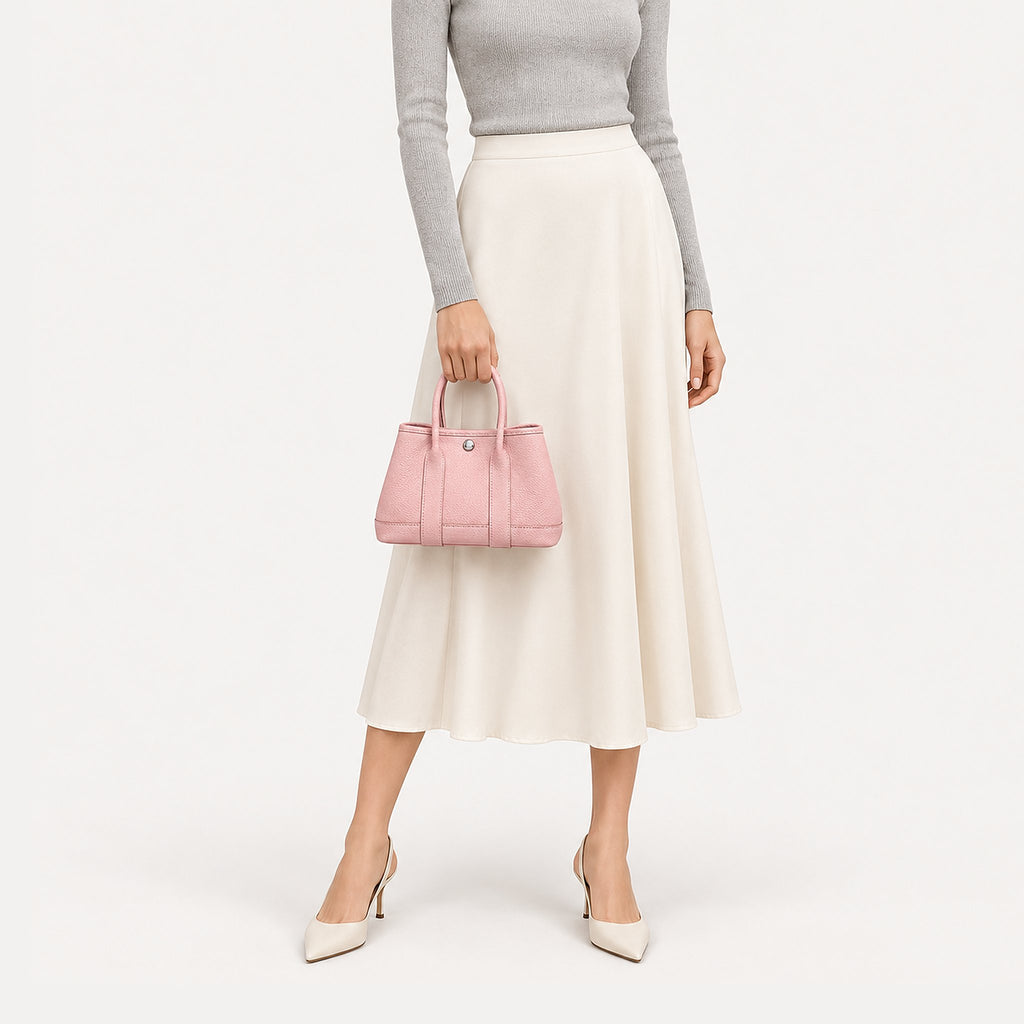 Weekday Tote Mini 23 cm open-top tote in baby pink carried by hand with a grey knit and cream midi skirt, model shot