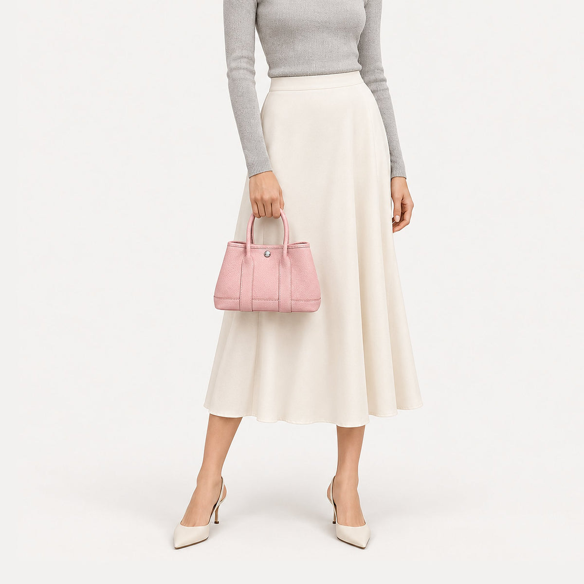 Weekday Tote Mini 23 cm open-top tote in baby pink carried by hand with a grey knit and cream midi skirt, model shot