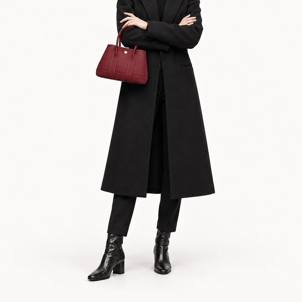 Weekday Tote Mini 23 cm open-top tote in burgundy carried by hand with a long black coat, model shot