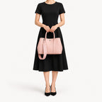 Weekday Tote Medium 30 cm open-top tote in baby pink held with both hands, included woven strap attached, styled with a black midi dress, model shot