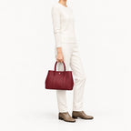 Weekday Tote Medium 30 cm open-top tote in burgundy carried by the top handles with an all-cream knit outfit, model shot