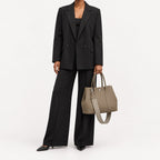 Weekday Tote Medium 30 cm open-top tote in khaki carried by hand with the included woven shoulder strap attached, worn with a black trouser suit, model shot