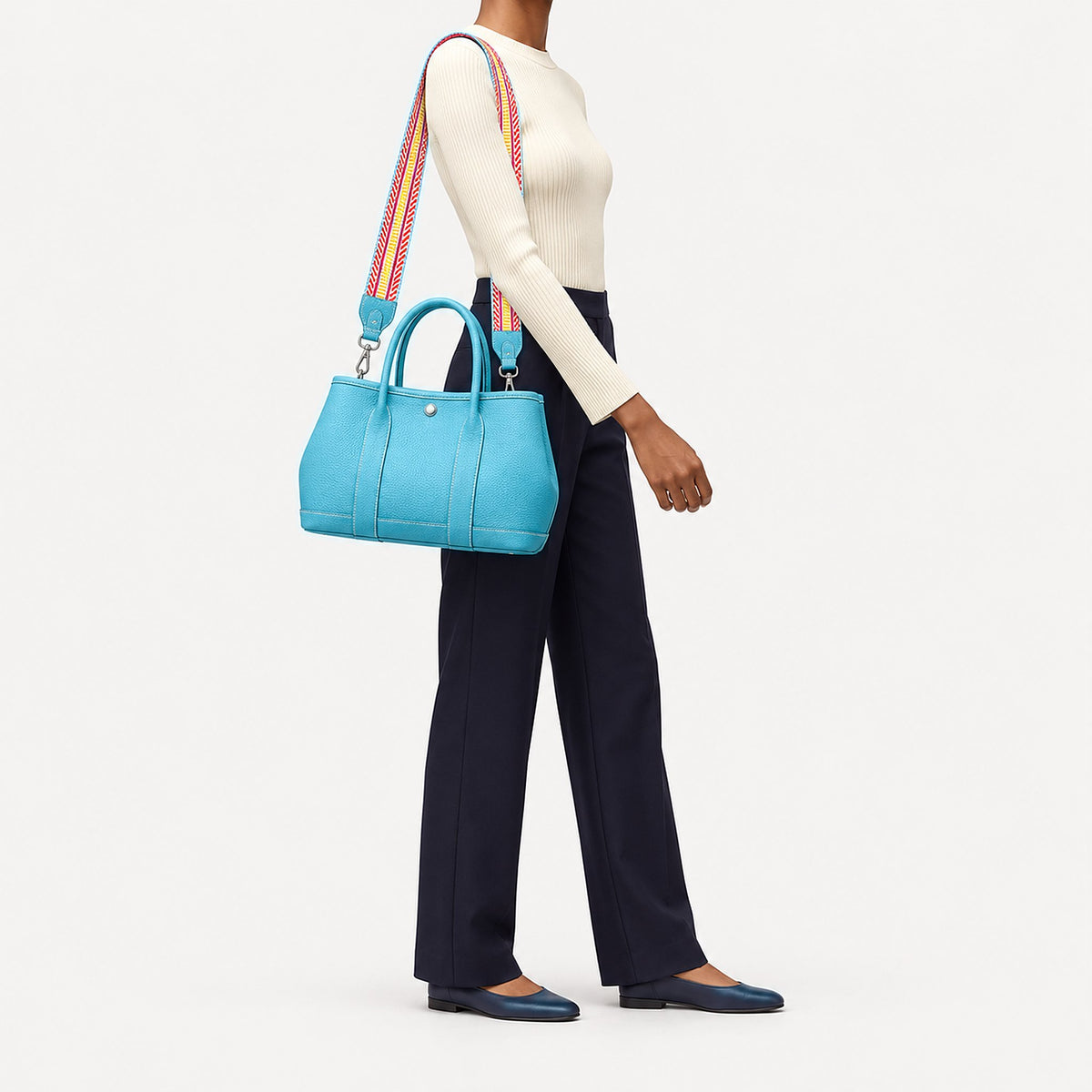 Weekday Tote Medium 30 cm open-top tote in sky blue worn on the shoulder with the included woven strap, styled with an ivory knit and navy trousers, model shot