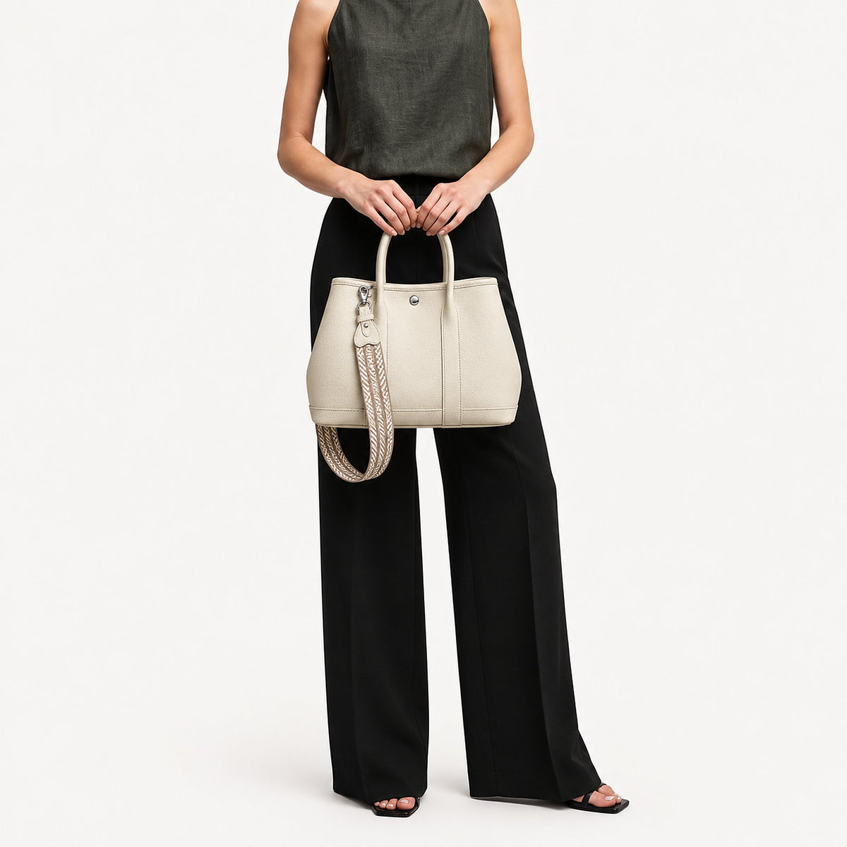 Weekday Tote Medium 30 cm open-top tote in white held with both hands, included woven strap attached, styled with a sleeveless top and black wide-leg trousers, model shot